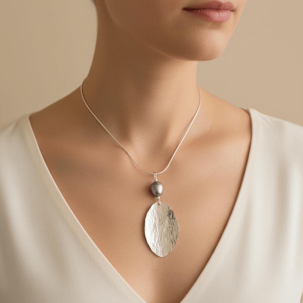 Close-up lifestyle shot of model wearing hammered silver leaf and baroque pearl necklace