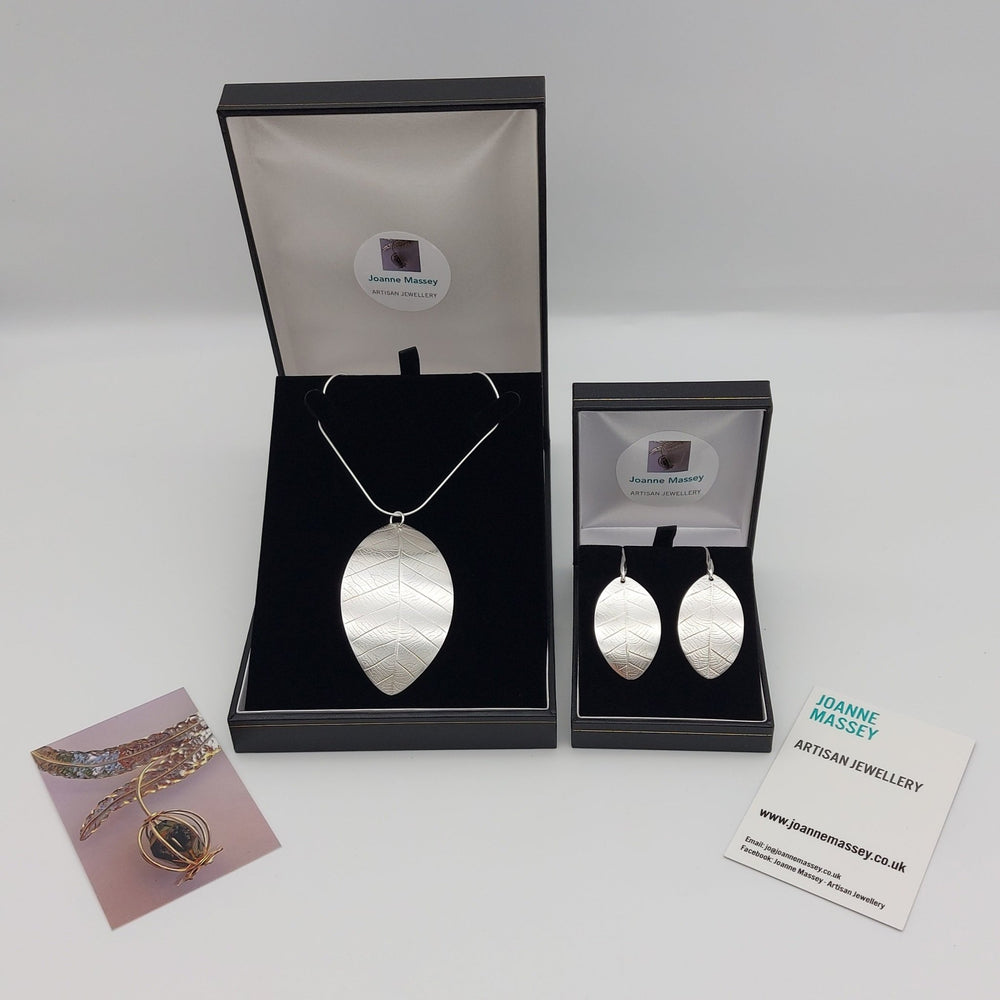 Silver leaf necklace and earrings set in open jewellery boxes with branded cards on white background