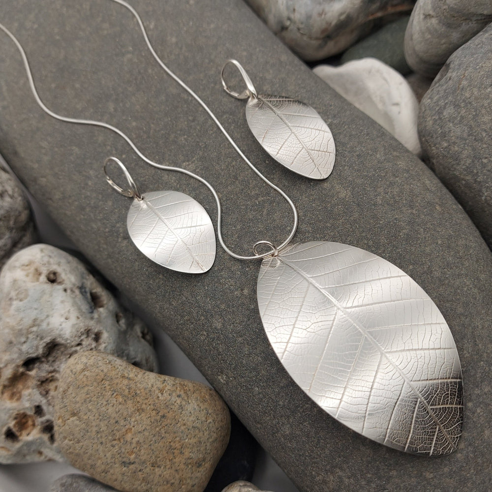 Silver leaf-shaped necklace and earrings jewellery set on a stone surface