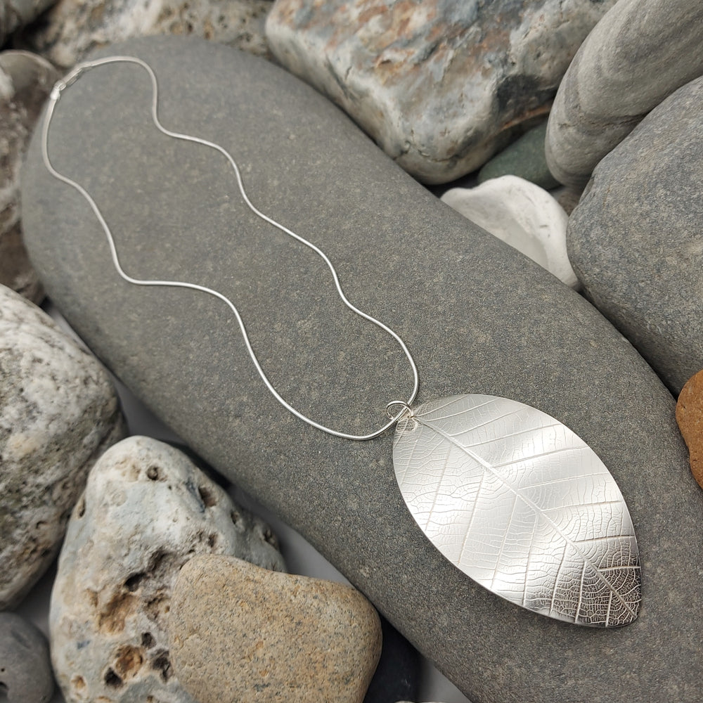 Silver leaf-shaped pendant on a chain lying on pebbles