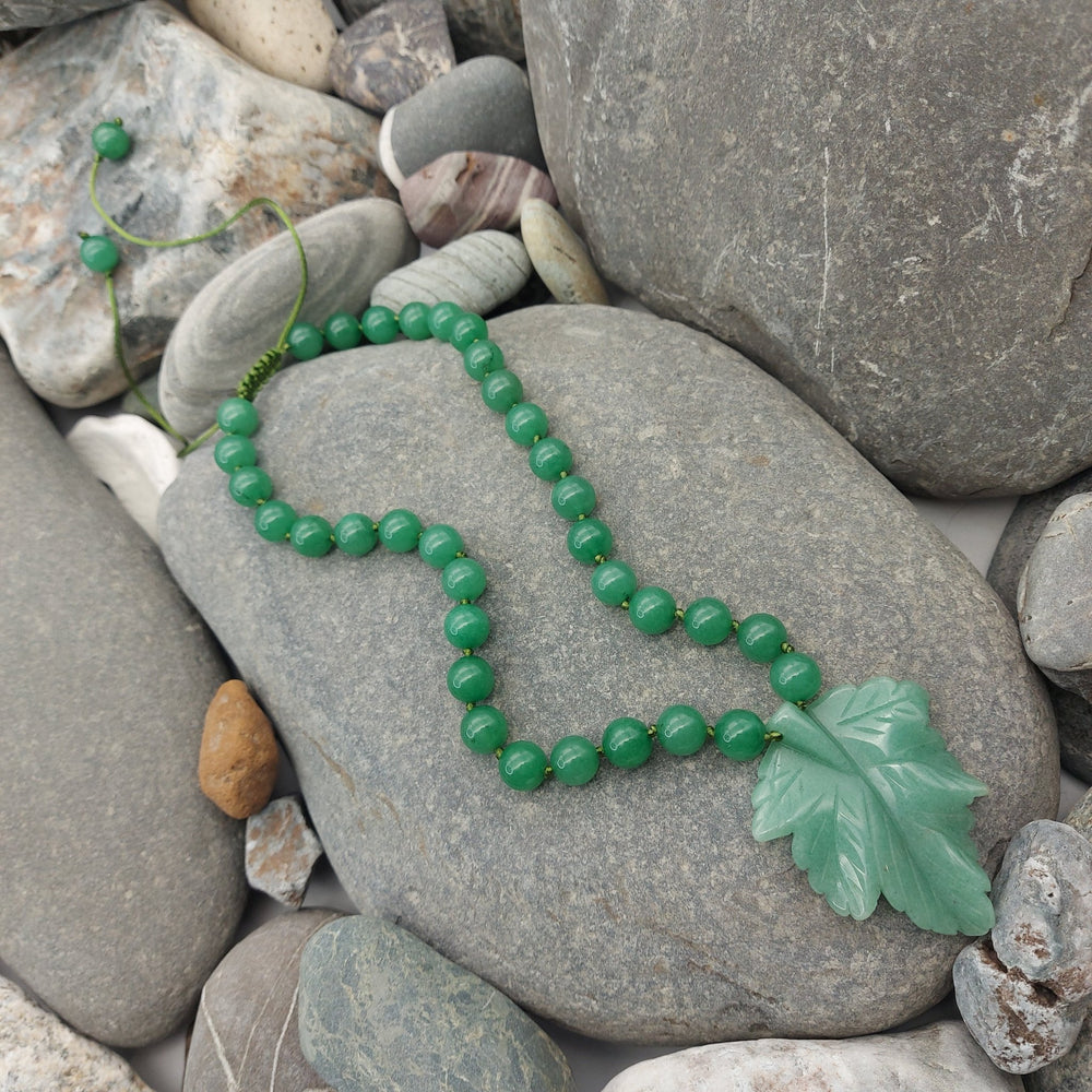 Handmade green aventurine necklace with carved leaf pendant and gemstone beads displayed on natural stones