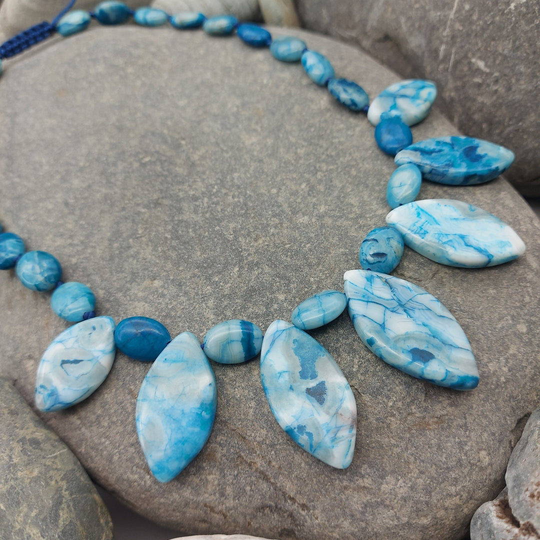 Close-up of marquise and oval Blue Crazy Lace Agate gemstones displayed on pebbles
