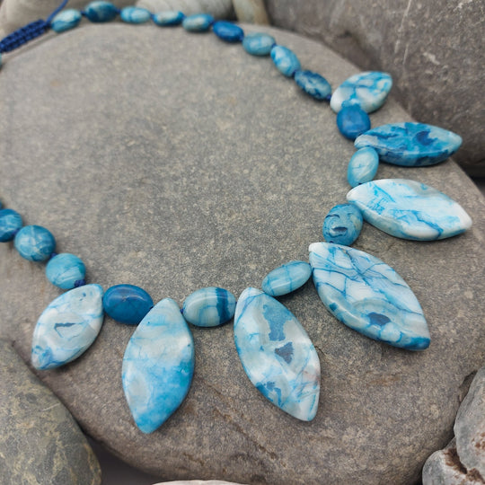 Close-up of marquise and oval Blue Crazy Lace Agate gemstones displayed on pebbles