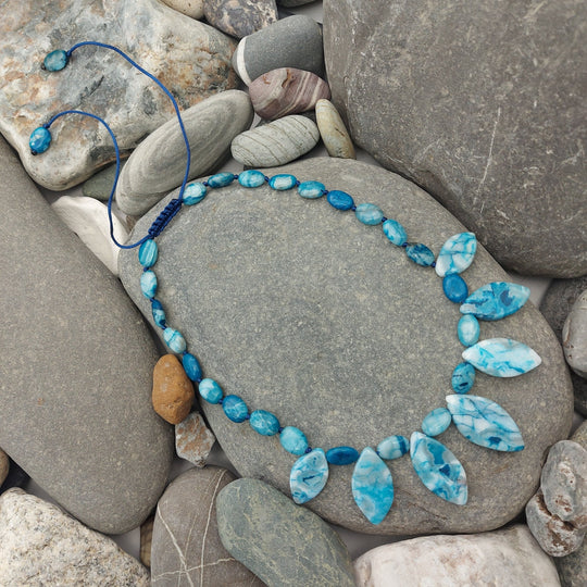 Blue Crazy Lace Agate statement necklace displayed on natural grey pebbles