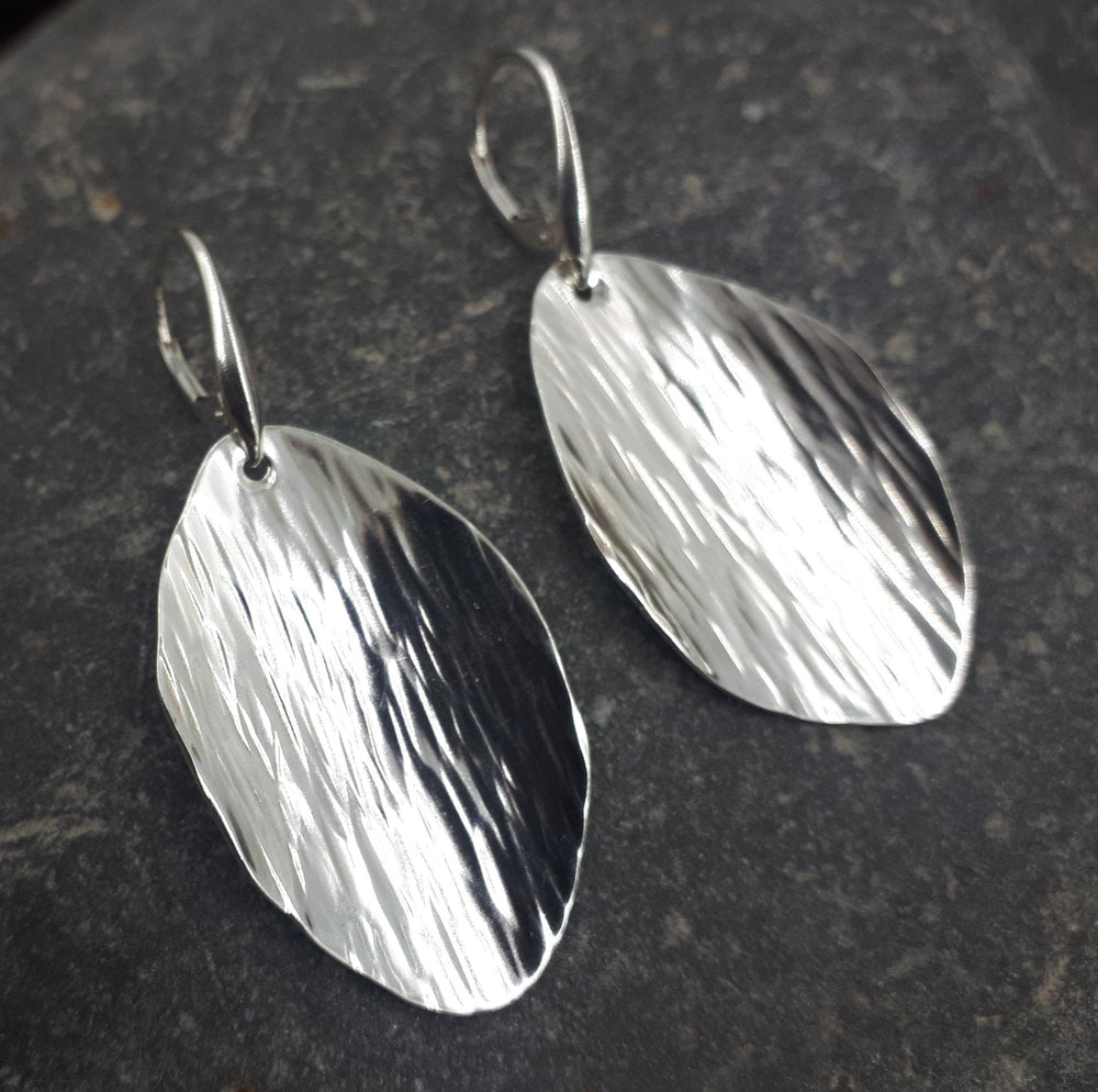 Pair of handmade sterling silver leaf earrings with bark texture on dark stone surface