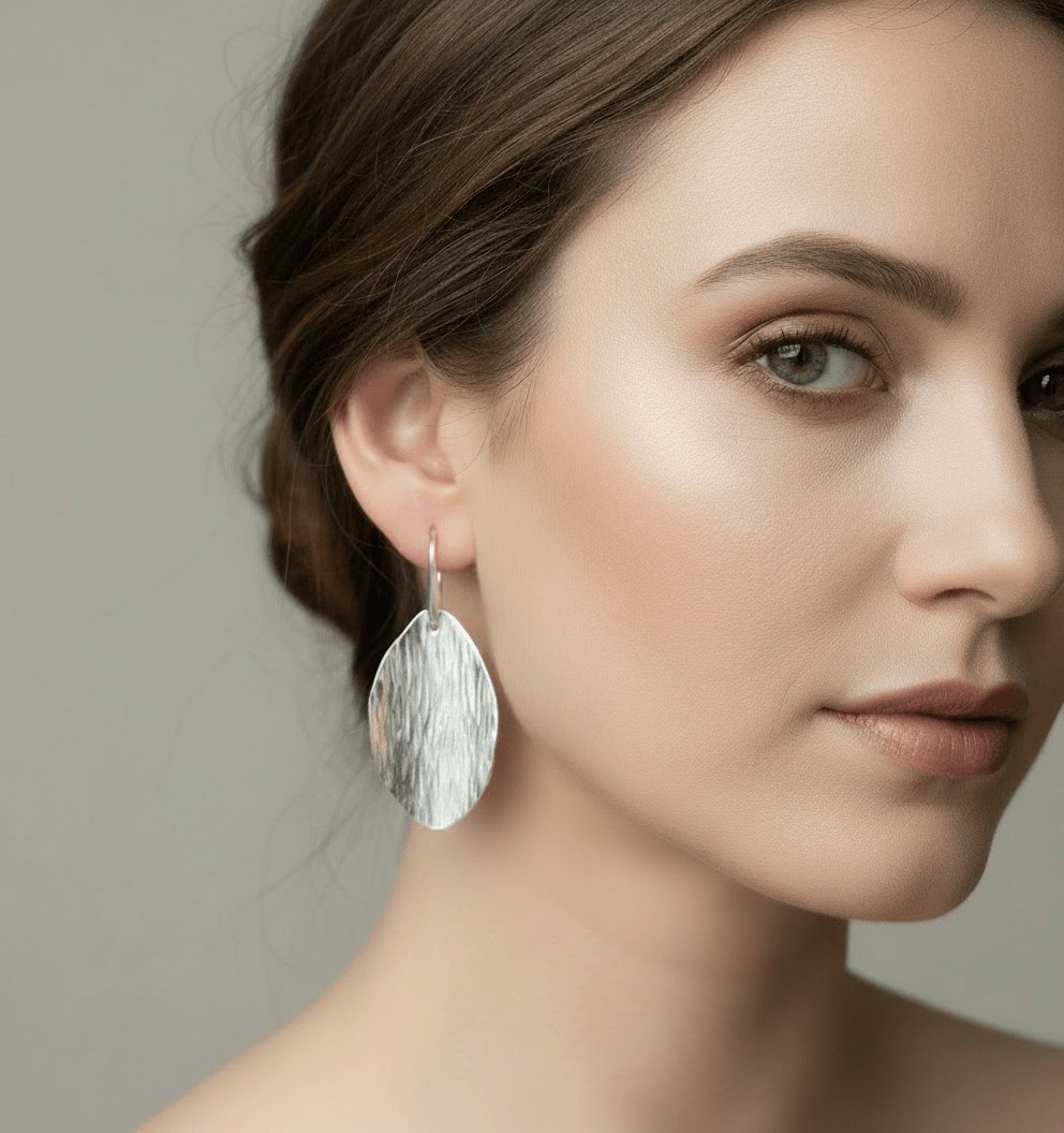 Close-up of woman wearing large sterling silver leaf earrings with bark texture against neutral background